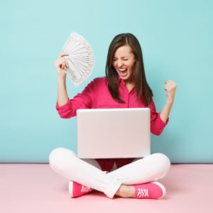 Full length portrait of young woman in rose shirt blouse, white pants sitting on floor hold money pc isolated on pink blue pastel wall background studio. Fashion lifestyle concept. Mock up copy space